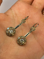 A pair of vintage-style gold-toned earrings with round bezel-set clear stones and ornate bar hooks, displayed on a person's palm.